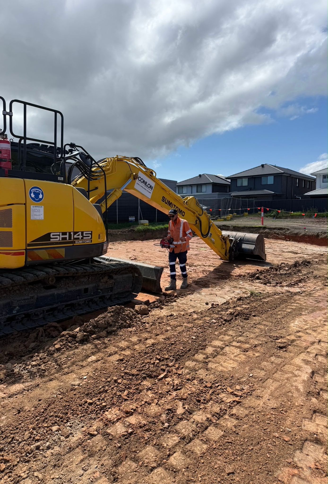 Conlon Contracting worker beside a Sumitomo SH145 excavator on a civil site