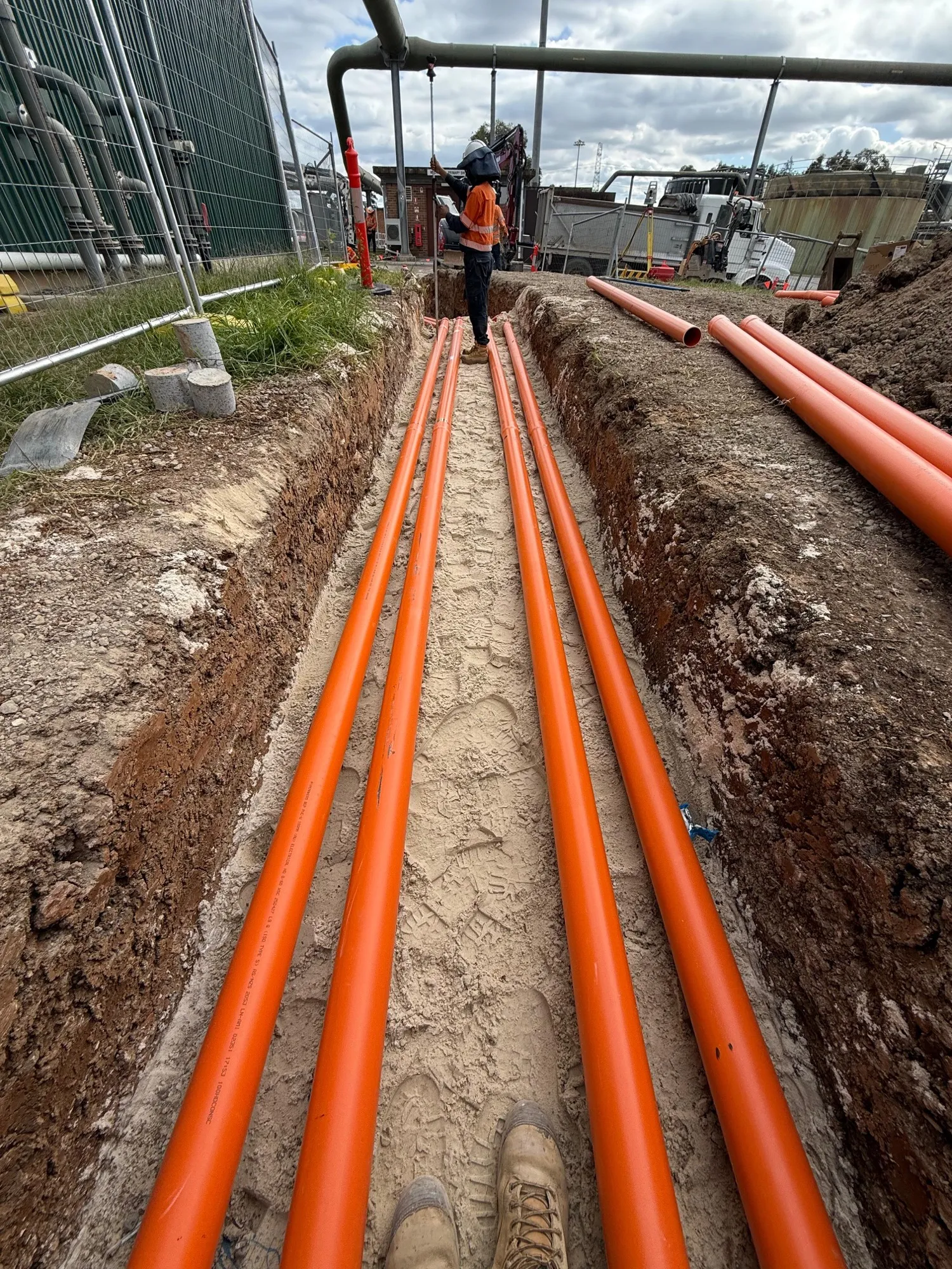 Four orange electrical conduits laid in a sand-bedded trench